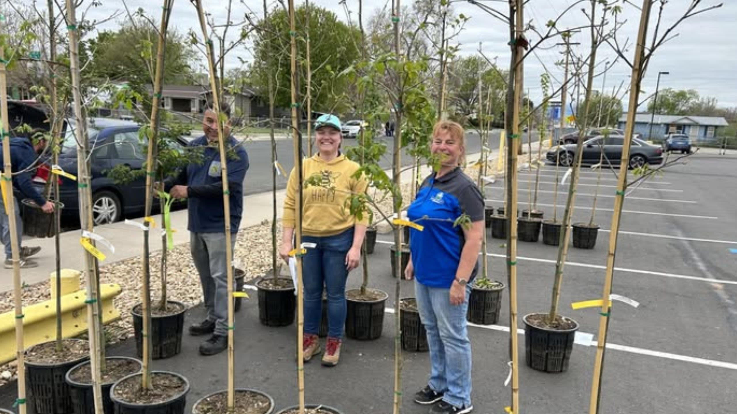 Several staff members posing next to young trees ready to go into the ground as part of the Tree Planting Program.