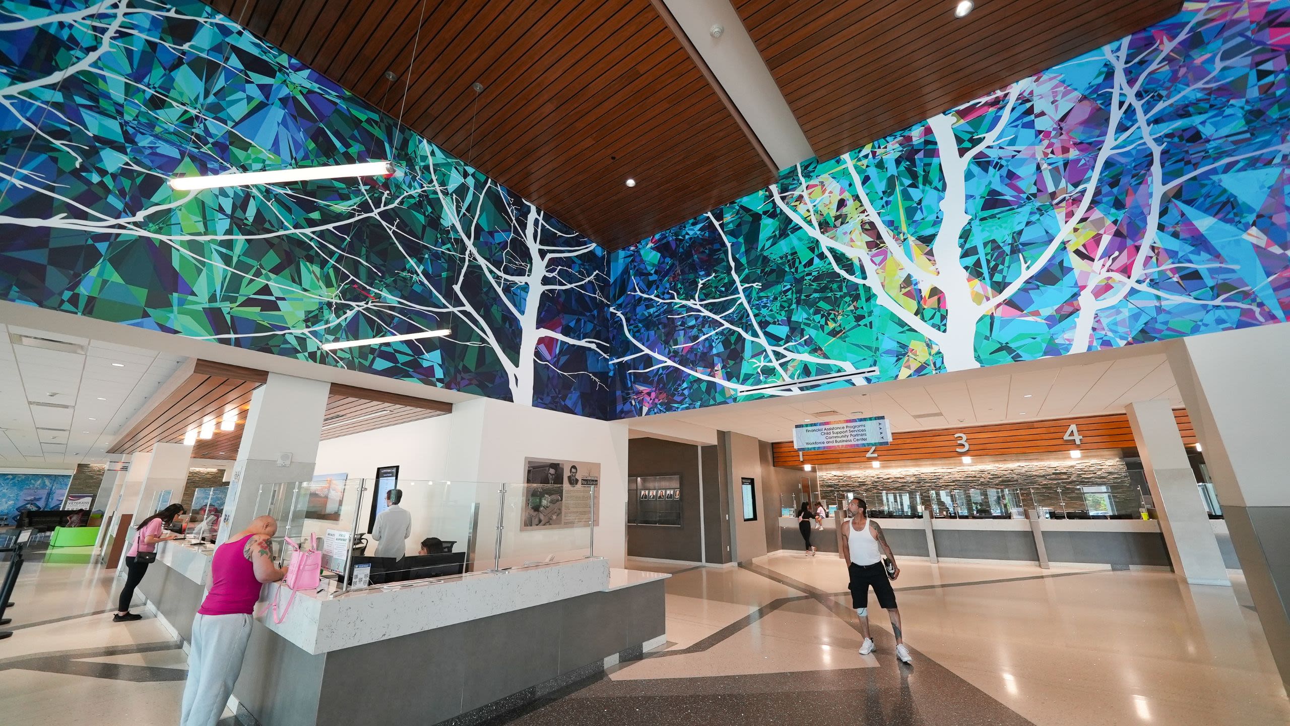Adams County residents utilizing services in the lobby of the Adams County Human Services Center, which features colorful murals, accessible help desks, resources, and more.